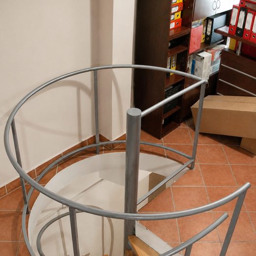 Pogled iz gornjeg ugla na sivu konstrukciju spiralnih stepenica sa drvenim gazištima i polukružnom ogradom galerije