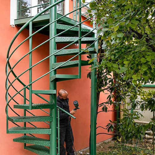 Zeleno spoljno spiralno metalno stepenište tokom postupka farbanja i zaštite u dvorištu