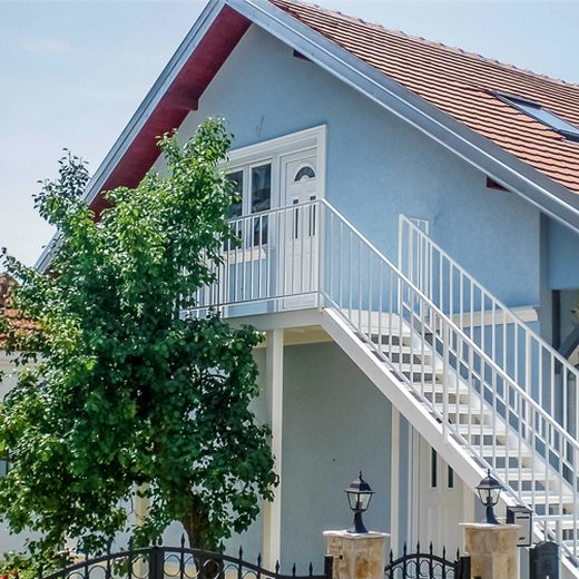 Bledo belo spoljno metalno stepenište sa podestom i zaštitnom ogradom za ulaz na sprat privatne kuće
