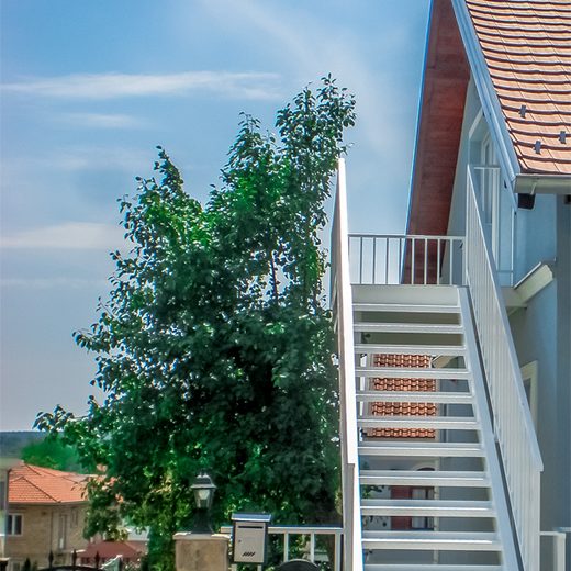 Pogled odozdo na spoljno čelično stepenište sa belom zaštitnom ogradom i protivkliznim gazištima