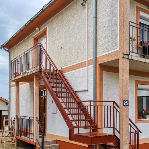 Braon spoljno dvokrako metalno stepenište sa podestom i vertikalnom ogradom za prilaz spratu kuće